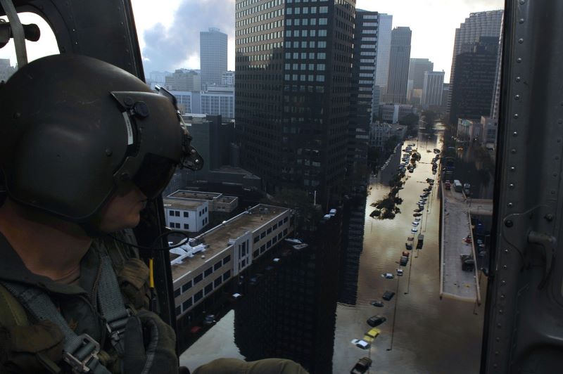 A uniformed person is overlooking flooding on a downtown city street from the vantage point of an aircraft.